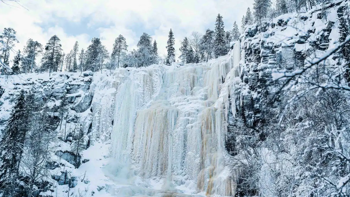 Photographer guide shooting travellers in front of a 60-metre frozen waterfall in Korouoma Canyon near Rovaniemi