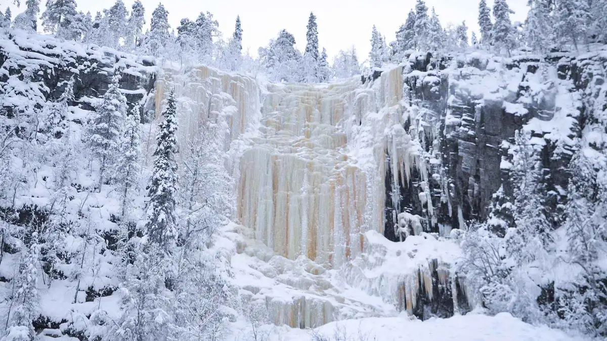 Wooden bridge over the frozen Auttikongas waterfall visited on a Korouoma Canyon frozen waterfalls day tour in Lapland